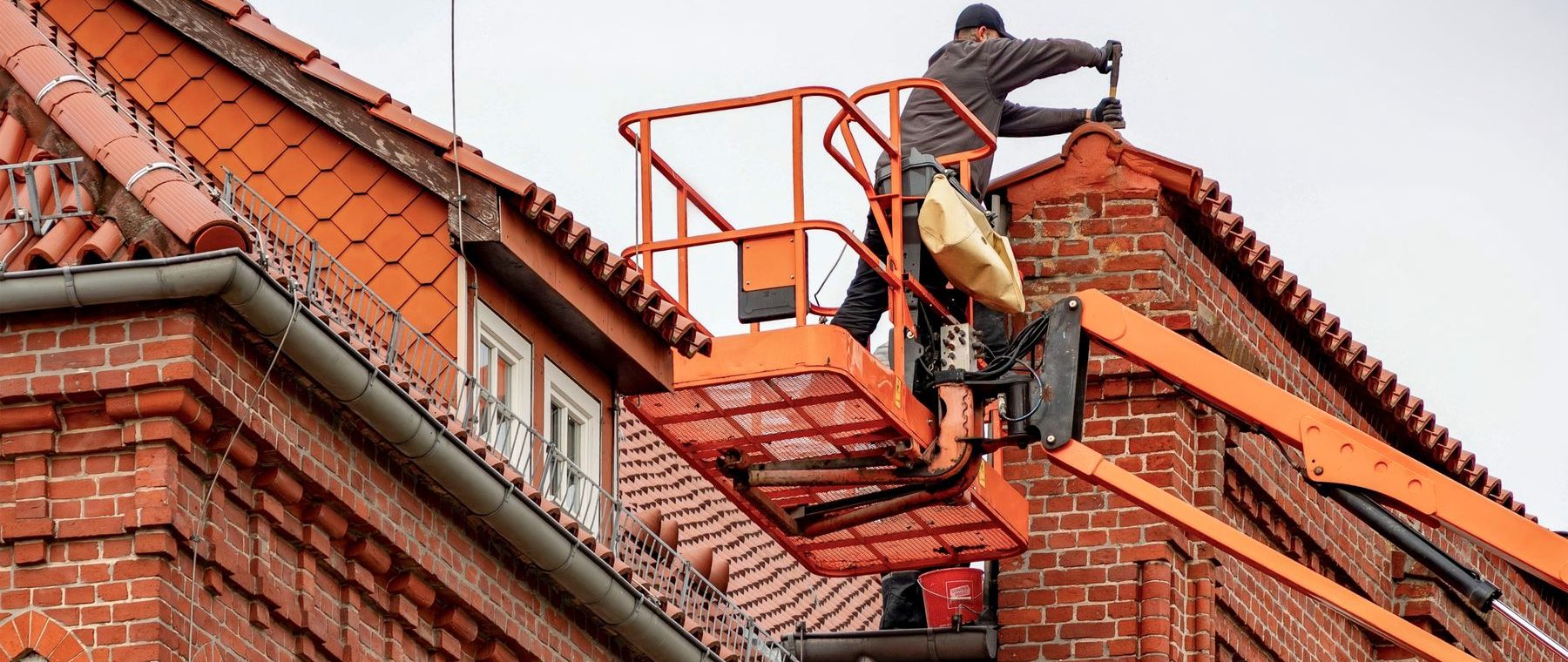 Dachdecker arbeitet von einer Hubarbeitsbühne am roten Ziegeldach eines Backsteinhauses