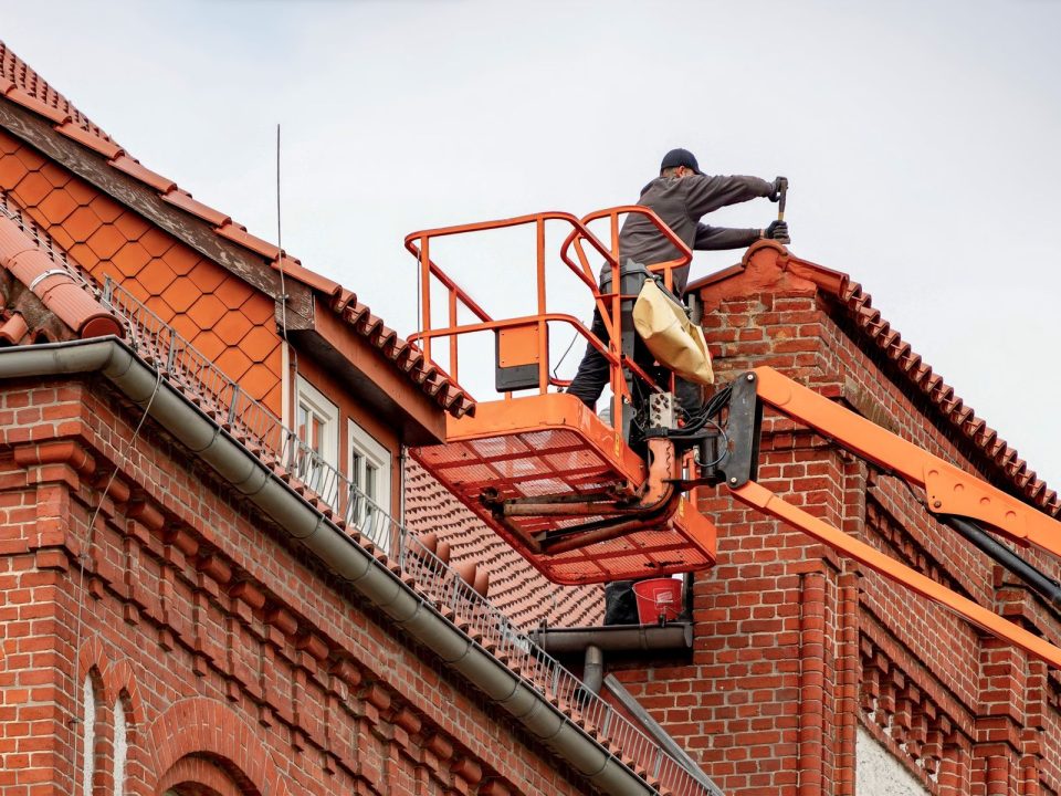 Dachdecker arbeitet von einer Hubarbeitsbühne am roten Ziegeldach eines Backsteinhauses